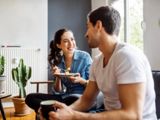 Junges Paar sitzt auf dem Sofa und die Frau isst Kuchen